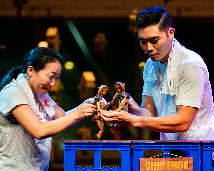 Two puppeteers in white shirts on stage, telling stories through their puppets.