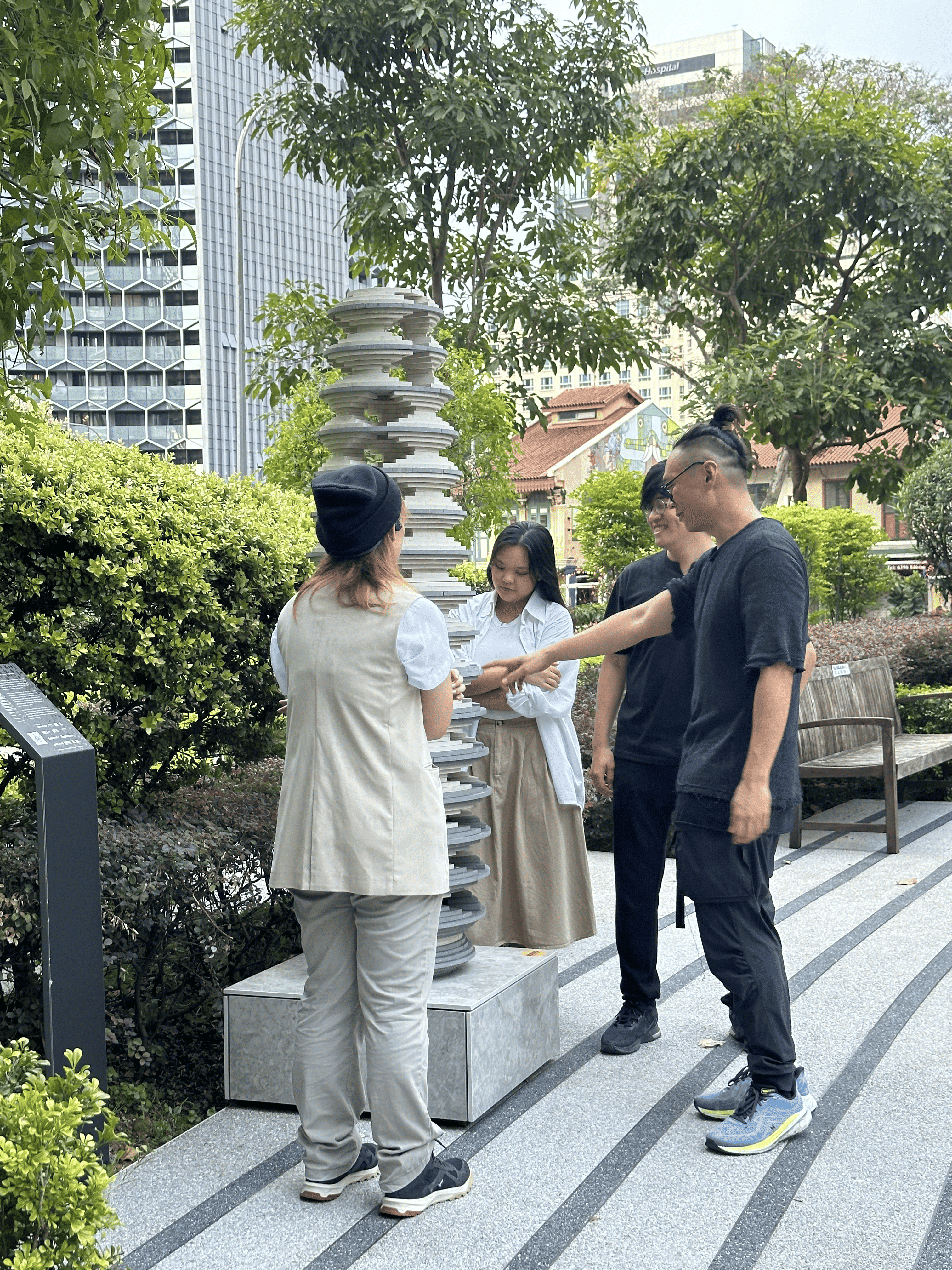 Side view of four people standing around the sculpture, admiring its layers. A man in black is pointing at the staggered surface of the disks