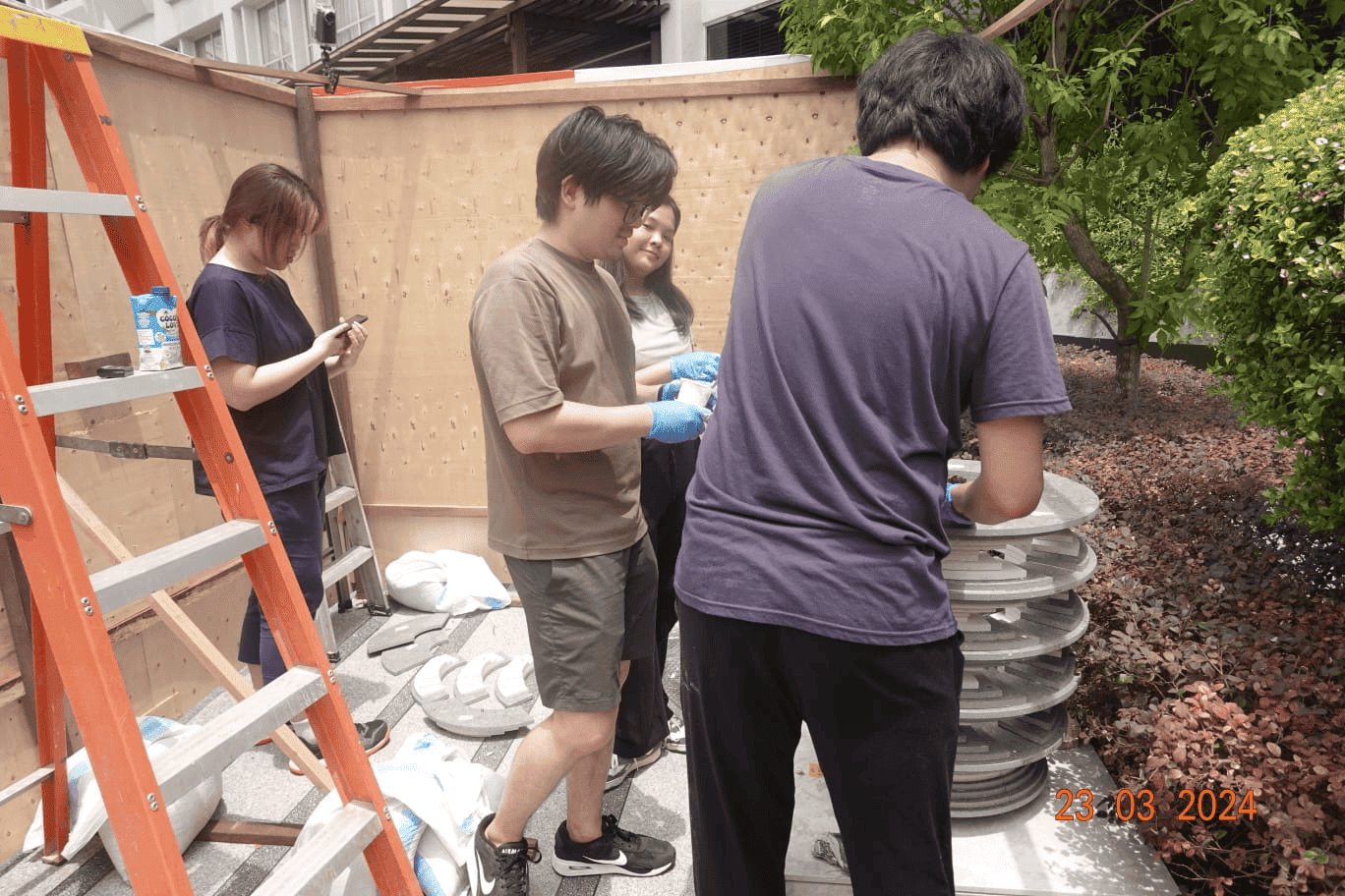 A behind-the-scenes photograph of people examining and working on the stacked disc sculpture, which is only completed till waist-level