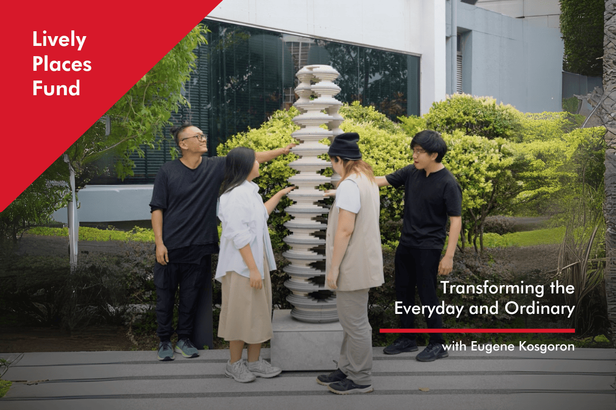 Four people stand around a tall, cylindrical sculpture of stacked concrete discs forming an artwork called Strata. The staggered discs create openings, revealing greenery in the background